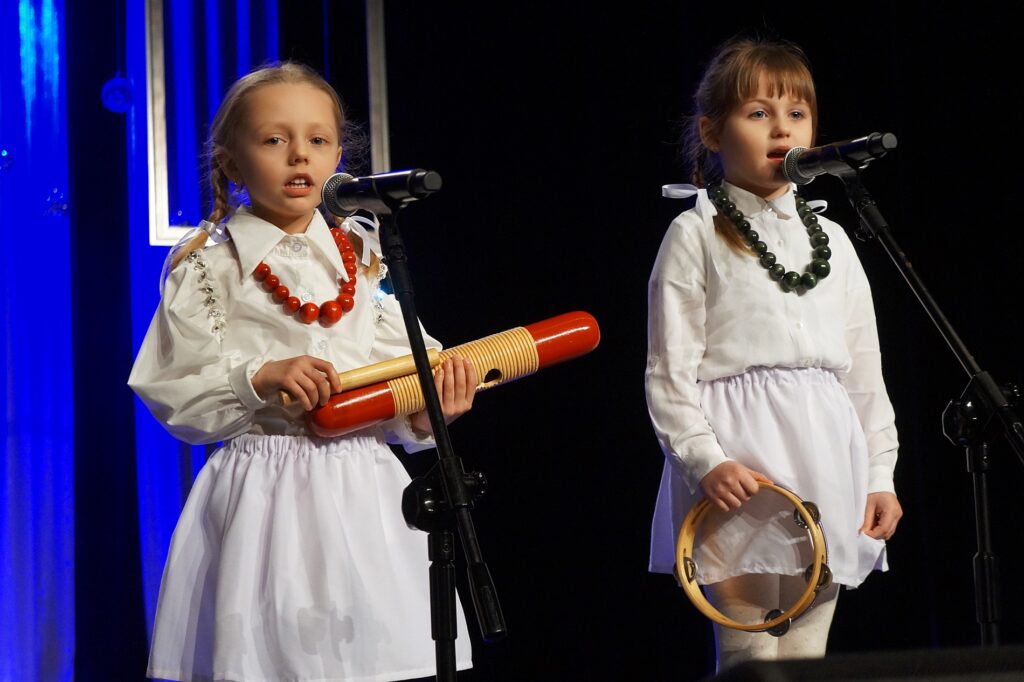 Dwie dziewczynki śpiewają kolędę. Występują z instrumentami muzycznymi.
