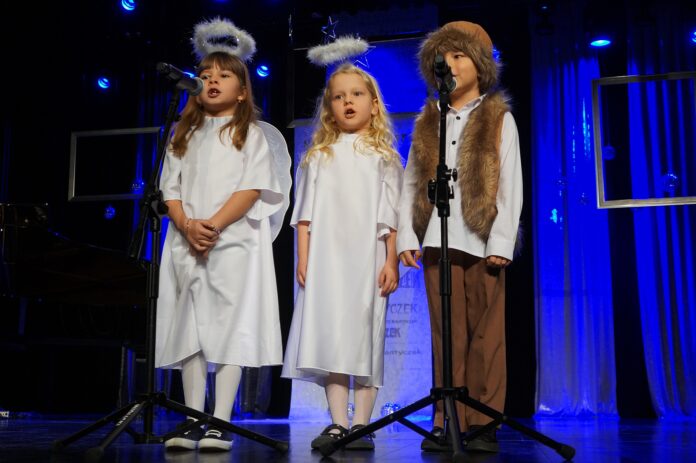 DSC00036 Dwie dziewczynki i chłopiec na scenie, śpiewają kolędę. Chłopiec przebrany jest za pastuszka natomiast dziewczynki za aniołki.