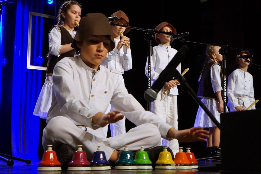Grupa dzieci występuje na scenie. Młodzi artyści grają na instrumentach muzycznych.