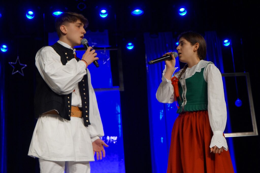 Młody chłopak i dziewczyna wspólnie wykonują utwór świąteczny na scenie.