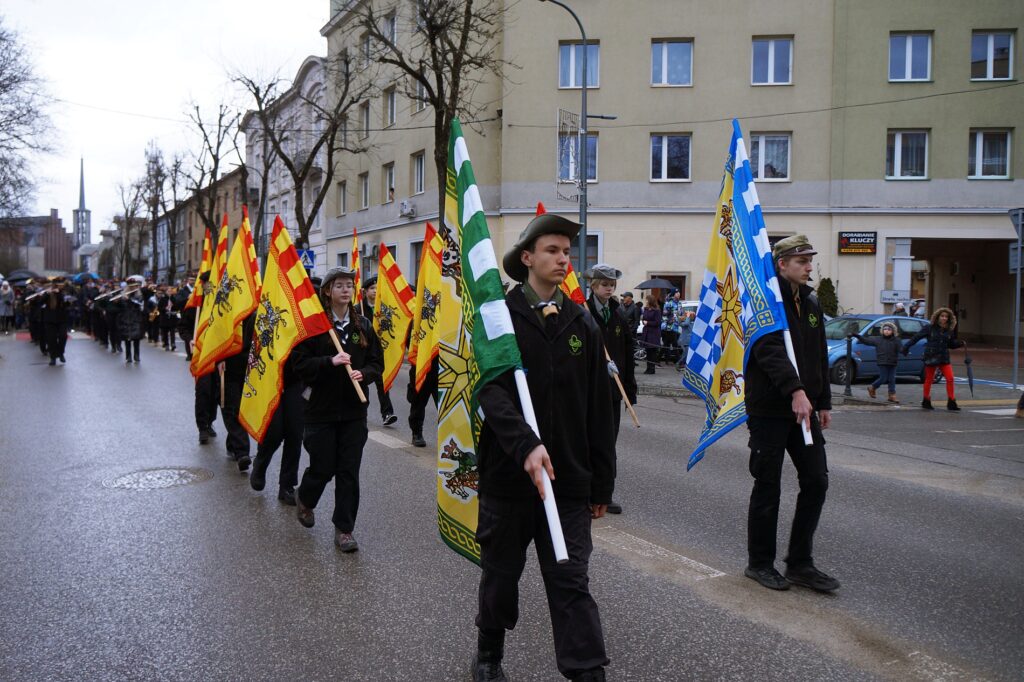 Harcerze maszerują w barwnym Orszaku. W dłoniach trzymają flagi symbolizujące Trzech Mędrców.