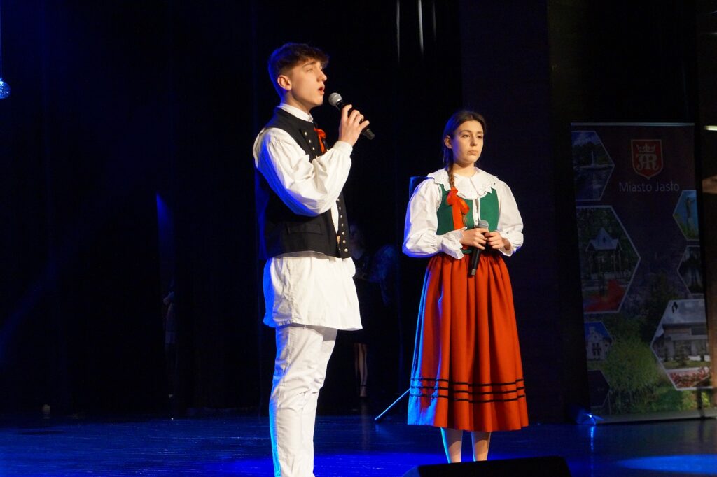 Dwóch wokalistów na scenie: dziewczyna i chłopak wspólnie śpiewają kolędę.