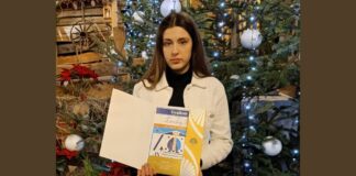 Karolina na międzynarodowym podium Na tle na drewnianych dekoracji i choinki ubranej w srebrne bombki stoi solista jasielskiego domu kultury karolina polak. ma biały rozpięty sweterek, pod spodem czarny golf i czarne spodnie. Przed sobą trzyma dyplom z konkurs kolęd