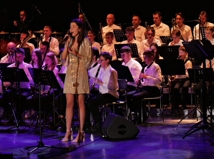 Koncert kolęd - Szkoła Muzyczna (1) Na scenie jasielskiego domu kultury gra młodzieżowa orkiestra. Muzycy ubrani są w białe koszule i czarne spodnie. Przed nimi stoi solistka Karolina Polak w złotej sukience i śpiewa kolędę do mikrofonu