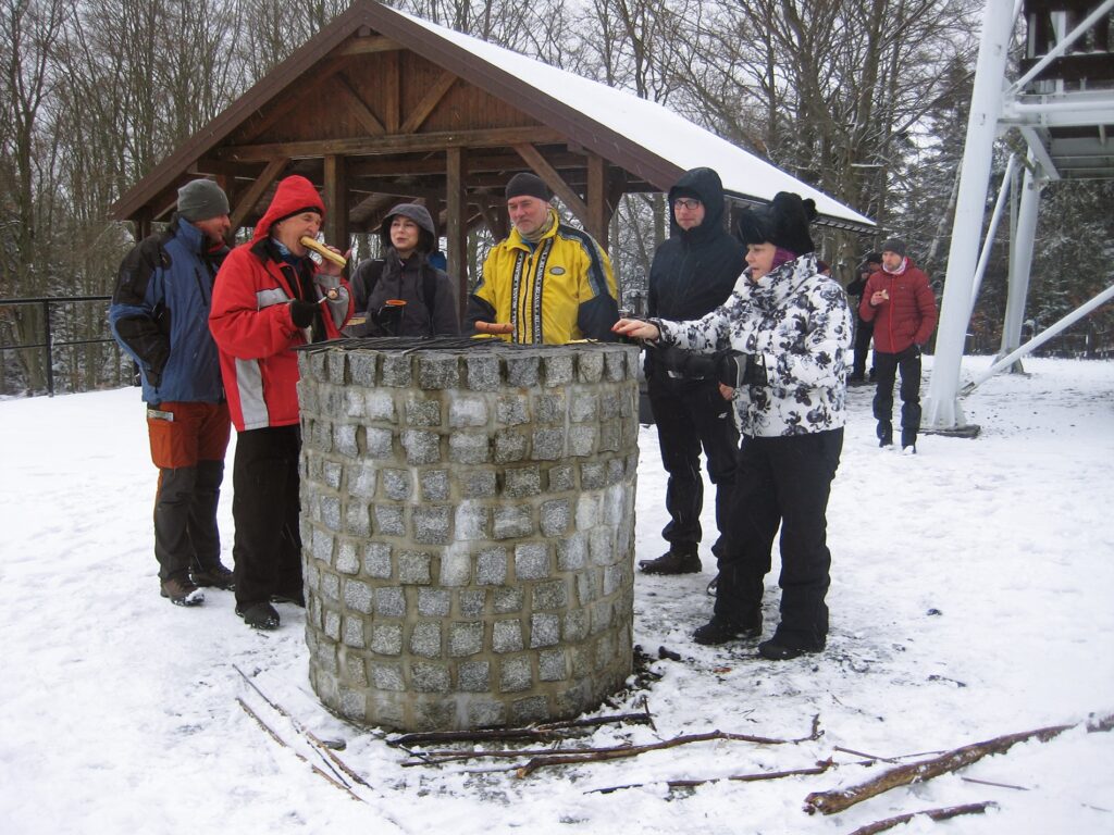 Grupa turystów ogrzewa się przy palenisku grillowym.