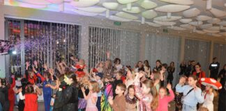 Bal w Krainie Fantazji Obraz zawiera: Dzieci w kostiumach balowych wraz z rodzicami bawią się wraz z Lady Famą łapiąc bańki mydlane.