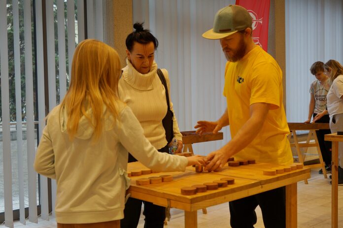 Trzy osoby: mężczyzna, kobieta i dziewczynka grają w jedną z drewnianych gier.