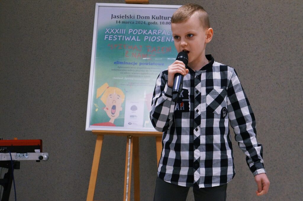 Chłopiec trzyma w dłoni mikrofon i śpiewa.