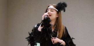 Młoda dziewczyna ubrana w czarny strój, śpiewa do mikrofonu.