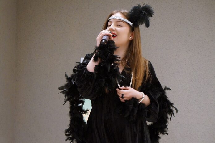 DSC01709 Młoda dziewczyna ubrana w czarny strój, śpiewa do mikrofonu.