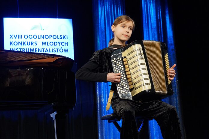 Dziewczynka siedzi i gra na akordeonie.