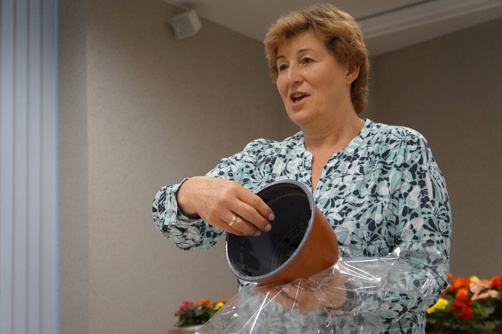 Pani Dorota prezentuje uczestnikom spotkania jak prawidłowo przygotować doniczkę na sadzonki.