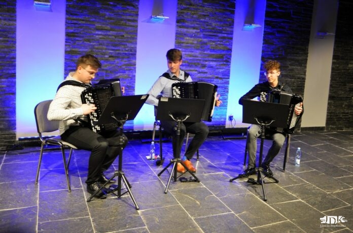 Koncert AccoArte_2 Obraz zawiera: trzech akordeonistów gra na instrumentach wpatrując się w zapisy nutowe umieszczone na pulpitach przed nimi.