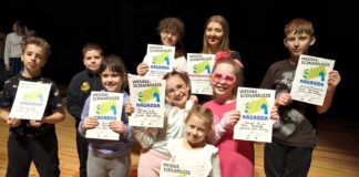 „Laboratorium absurdów…” z główną nagrodą dziecięca grupa teatralna wraz ze swoją instruktorką stoi na scenie z dyplomami za zwycięstwo w konkursie teatralnym