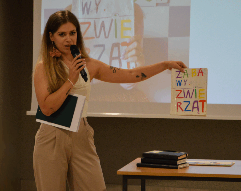 Eliza Banaś trzyma w ręku książkę, którą zrobiła jako dziecko. Książka ma kolorową okładkę z napisem "zabawy zwierząt"