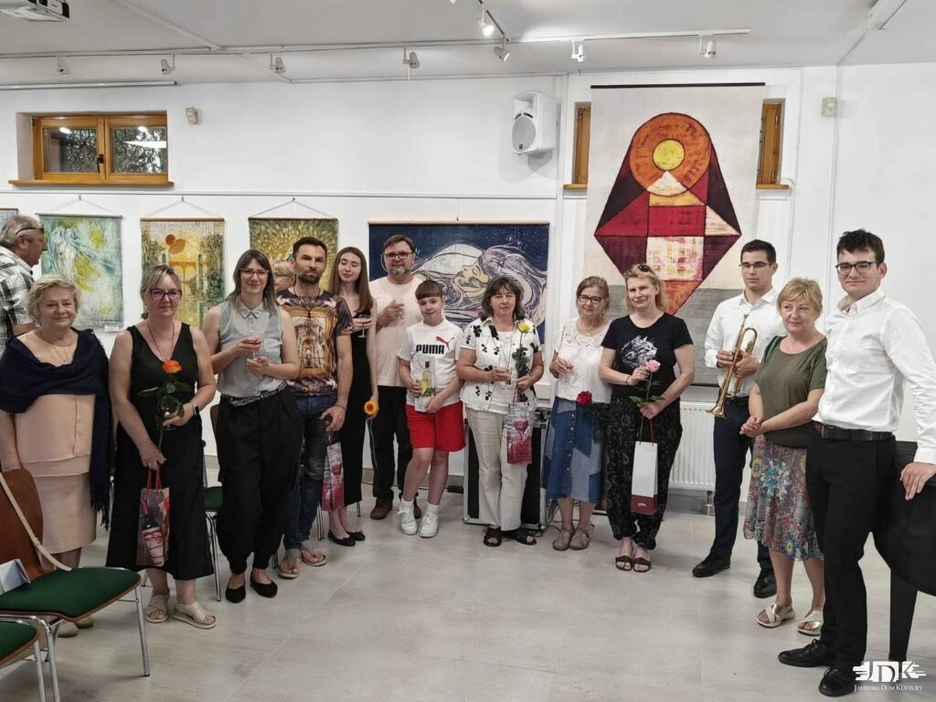 grupa uczestników wernisażu na tle kolorowych batików