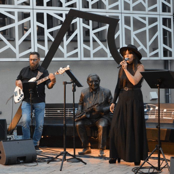 Koncert przy ławeczce Muzycy przy ławeczce. po środku pomnik Dudusia