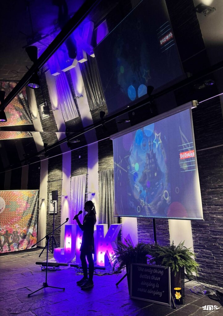 uczestniczka domówki śpiewa karaoke, w tle ekran z wyświetlanym tekstem