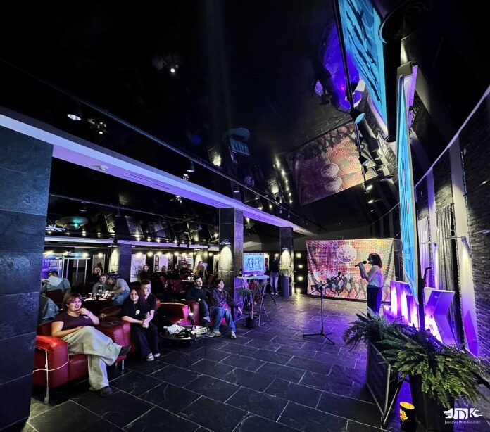 uczestniczka domówki śpiewa karaoke, w tle ekran z wyświetlanym tekstem oraz publiczność