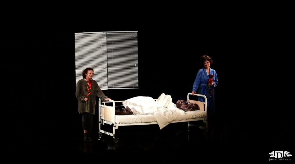 aktorki stoją po bokach łóżka z różami