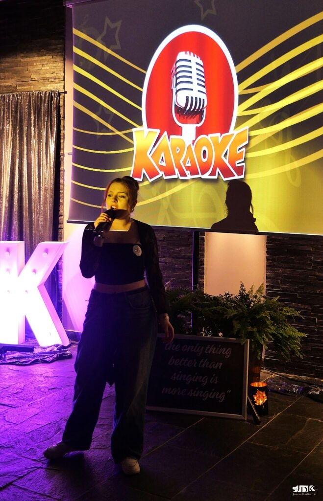 uczestniczka domówki śpiewa karaoke, w tle ekran z wyświetlanym tekstem