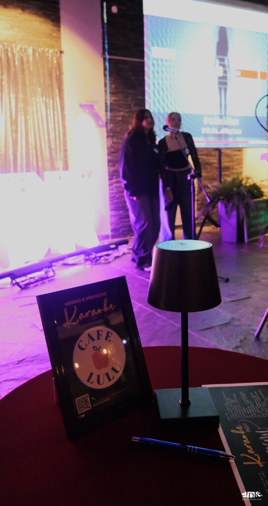 na pierwszym planie logo Cafe Lulu z lampką, na drugim planie duet