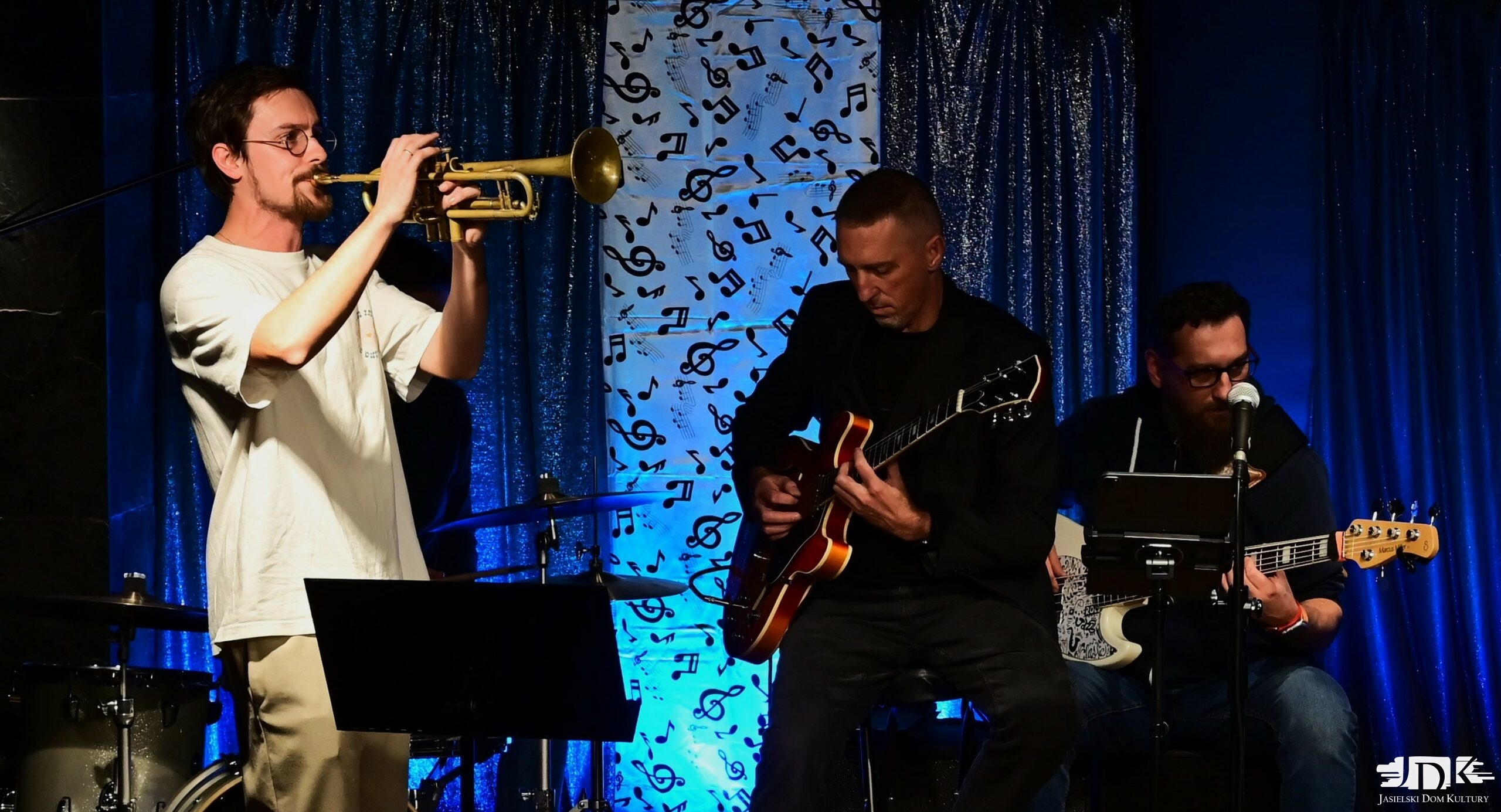 muzyk grający na trąbce oraz dwoje gitarzystów na drugim planie
