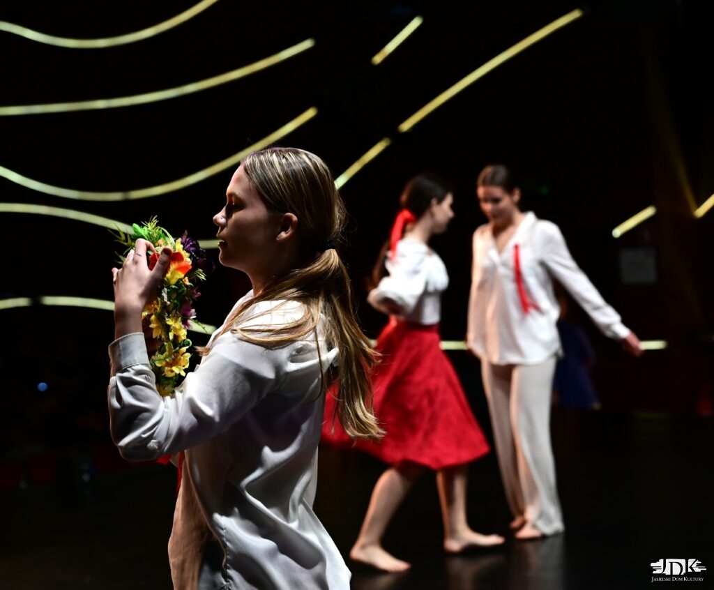 tancerka z wiankiem w dłoni, w tle para w ludowych strojach