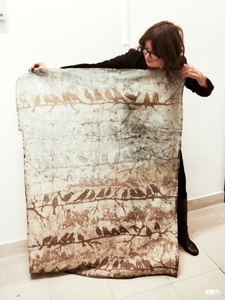 pani prezentuje duży batik w kolorach brązu z ptakami