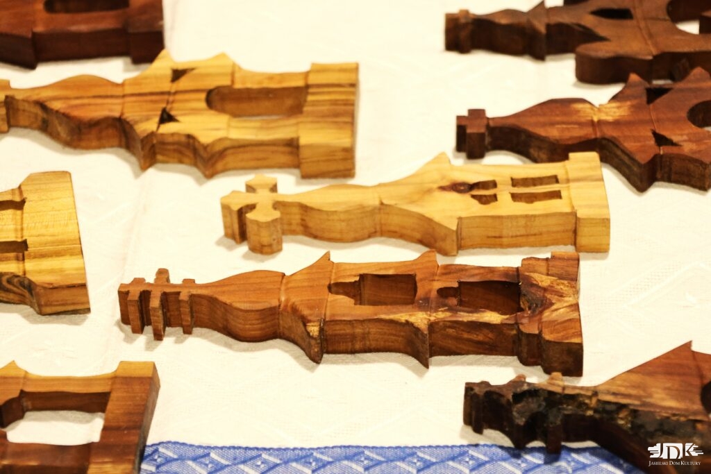 rzeźbione płaskie kapliczki leżące na białym obrusie z niebieską lamówką