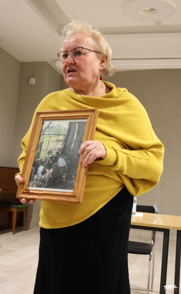 Pani Marchewka trzyma zdjęcie w drewnianej ramie, przedstawiające Pana Zbigniewa Marchewkę w otoczeniu pięciu kóz