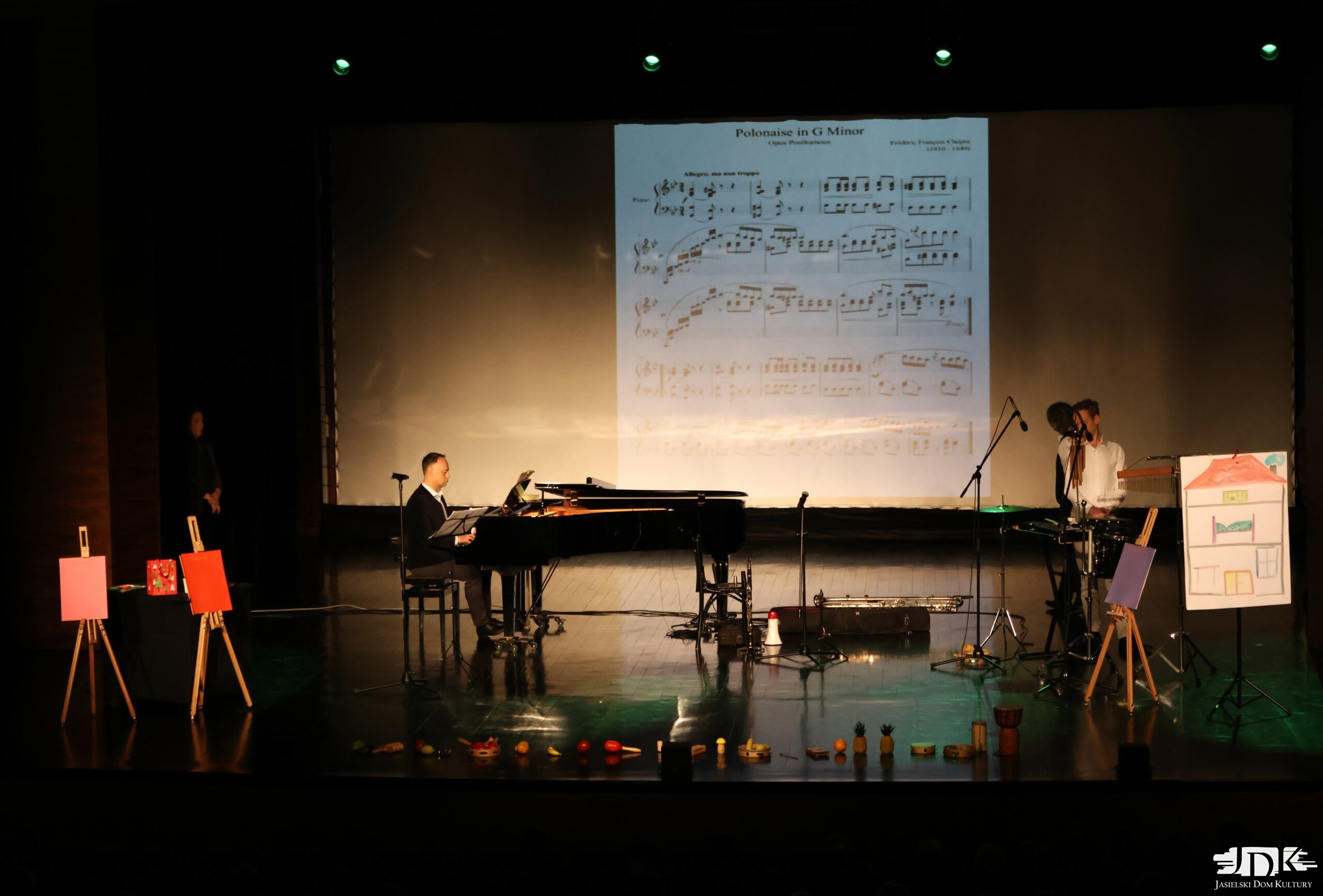 na scenie muzyk grający na fortepianie, a w tle wyświetla się partytura Chopina Polonez G Dur