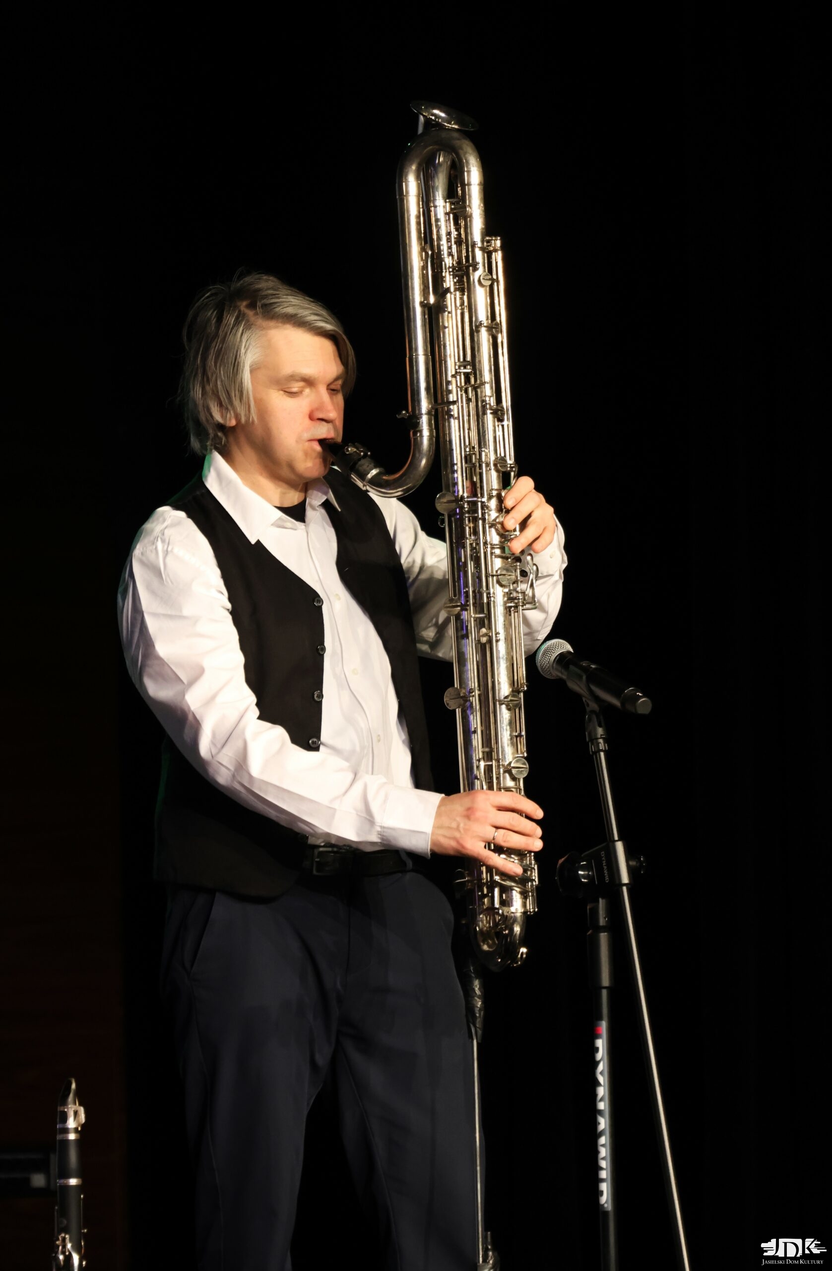 muzyk w białej koszuli i kamizelce grający na klarnecie basowym