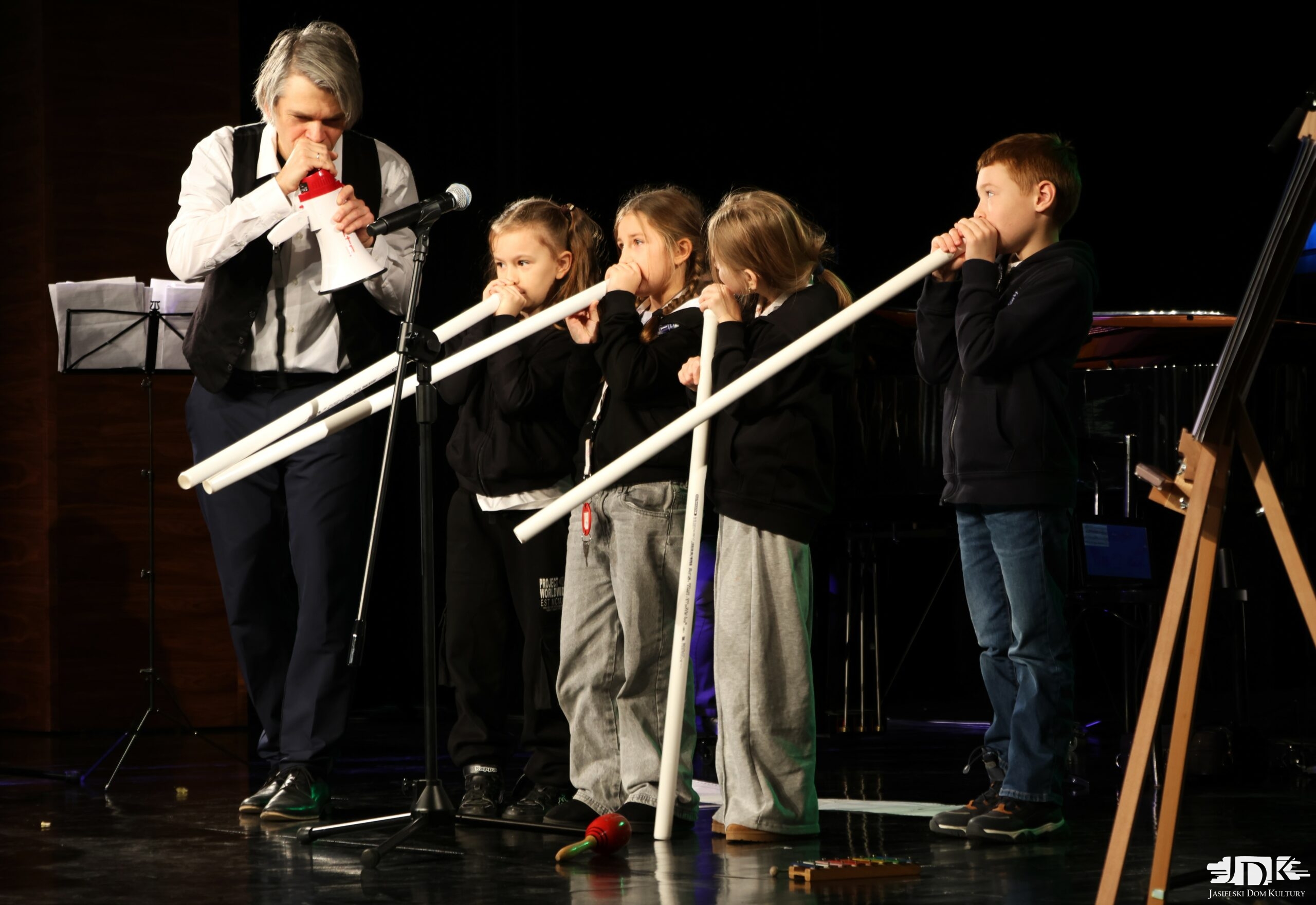 czworo dzieci grających na długich tubach oraz muzyk mówiący do megafonu