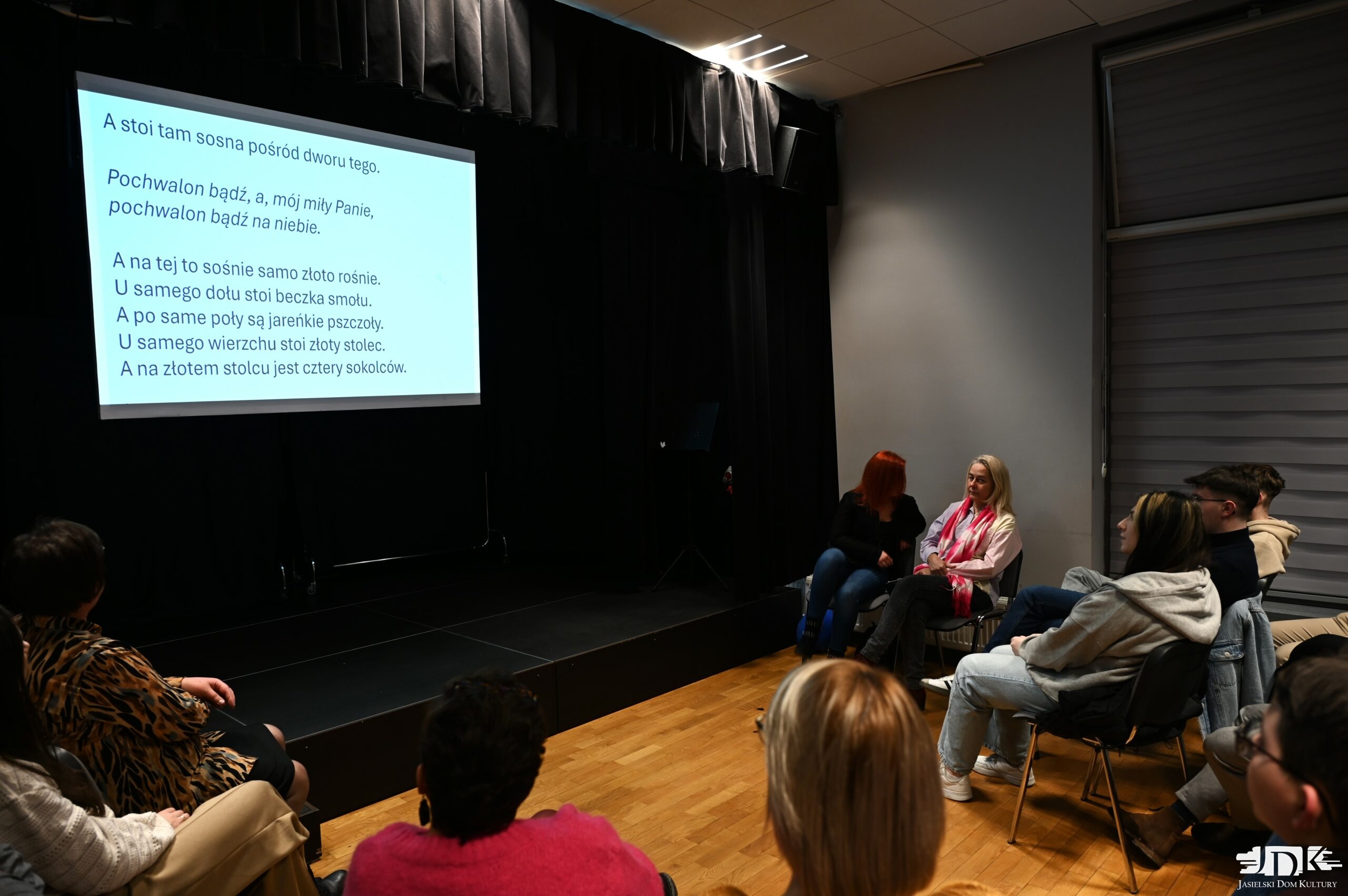 grupa uczestników warsztatów patrząca w ekran, na którym wyświetla się drobno tekst kolędy