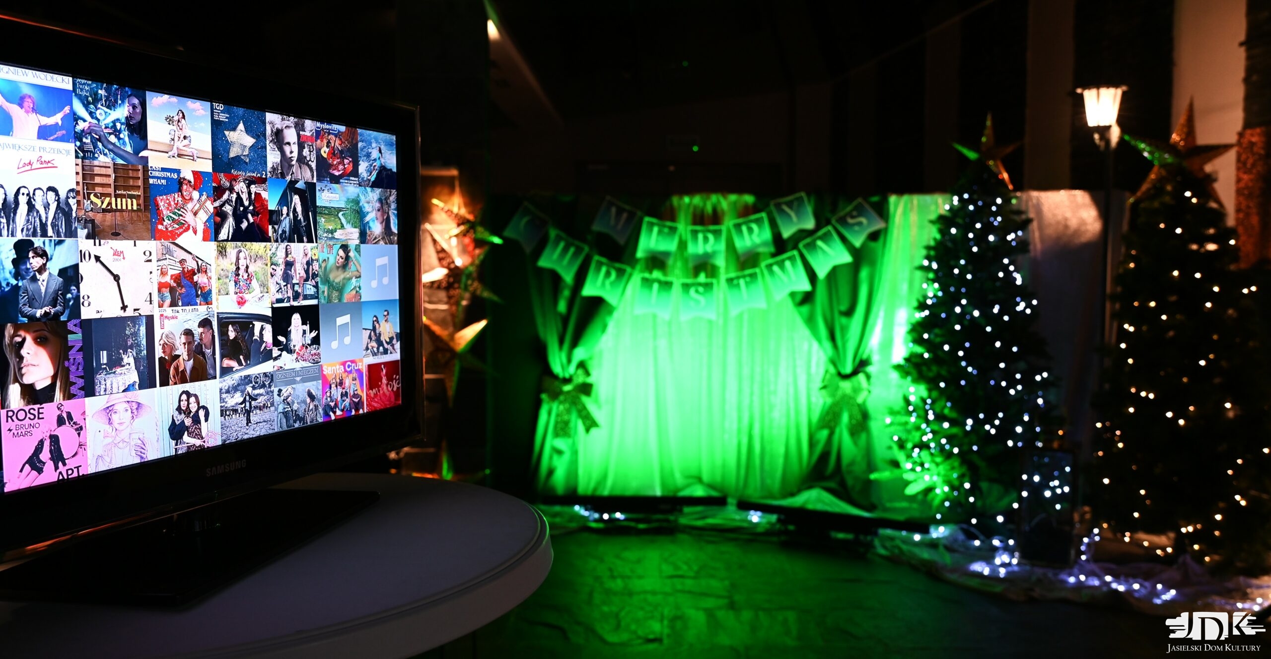 zimowa aranżacja z dwoma choinkami i ekranem wyświetlającym piosenki