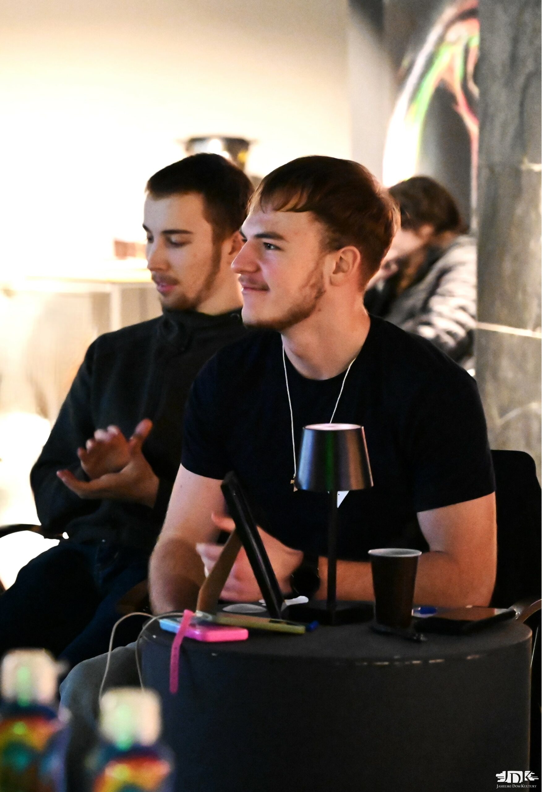 dwoje uczestników karaoke ubranych w czarne bluzki uśmiechają się, słuchając piosenek