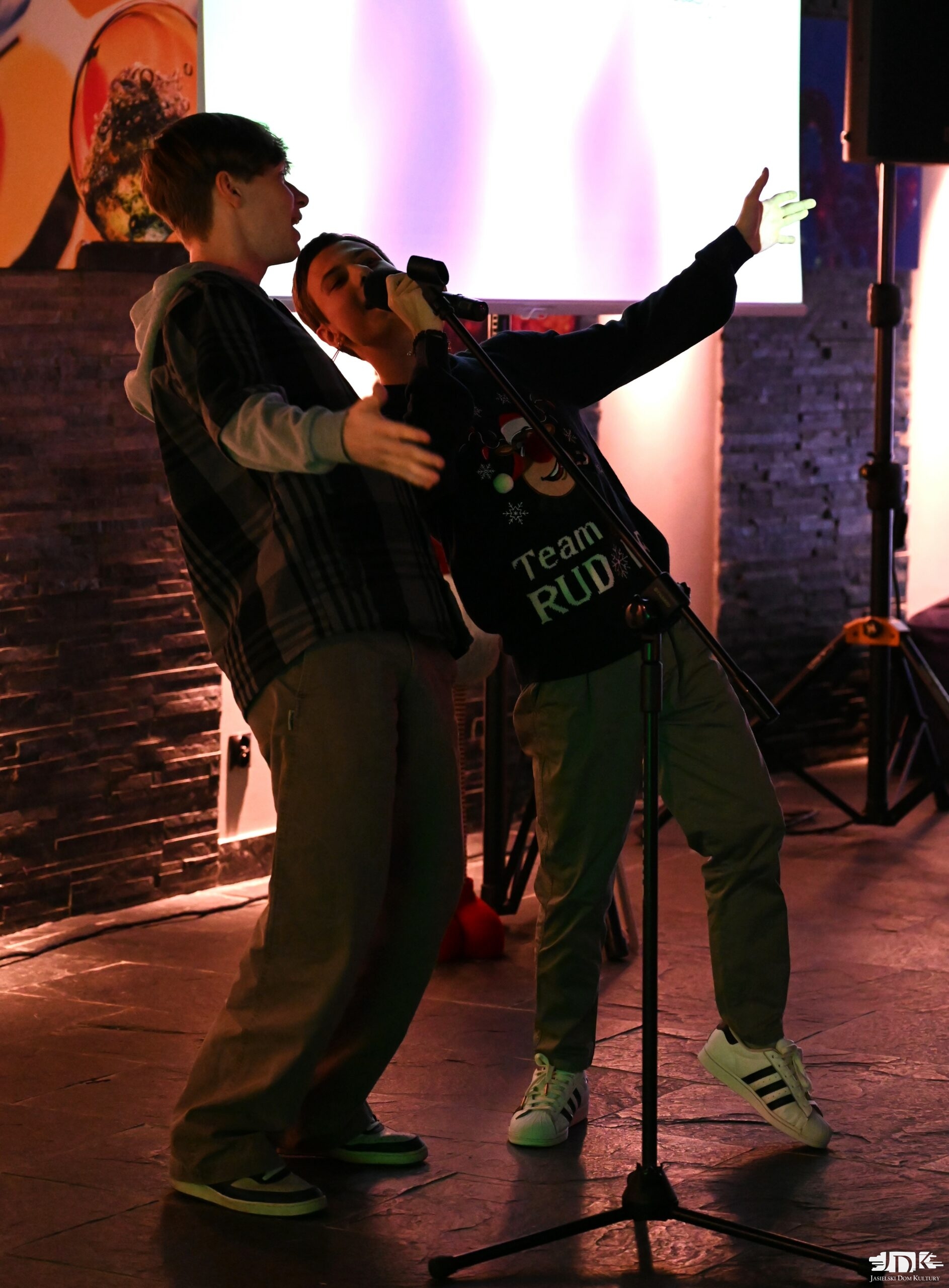 dwóch chłopaków śpiewa do mikrofonu, w tle jasny ekran karaoke