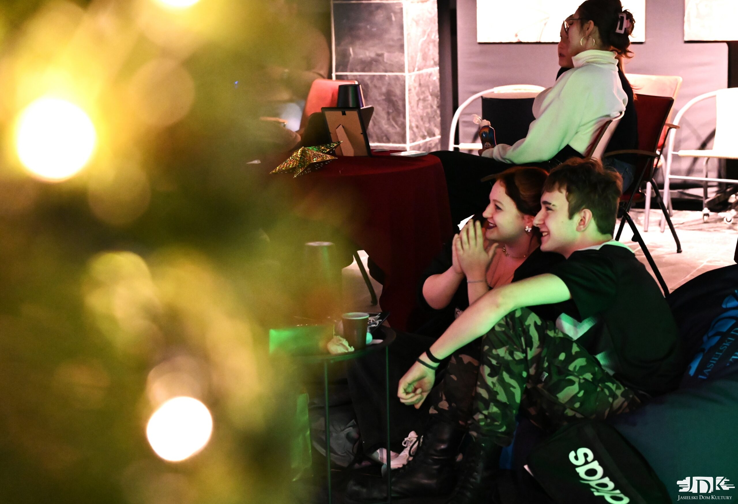 para siedząca na pufach, w tle dwie dziewczyny rozmawiające przy stoliku