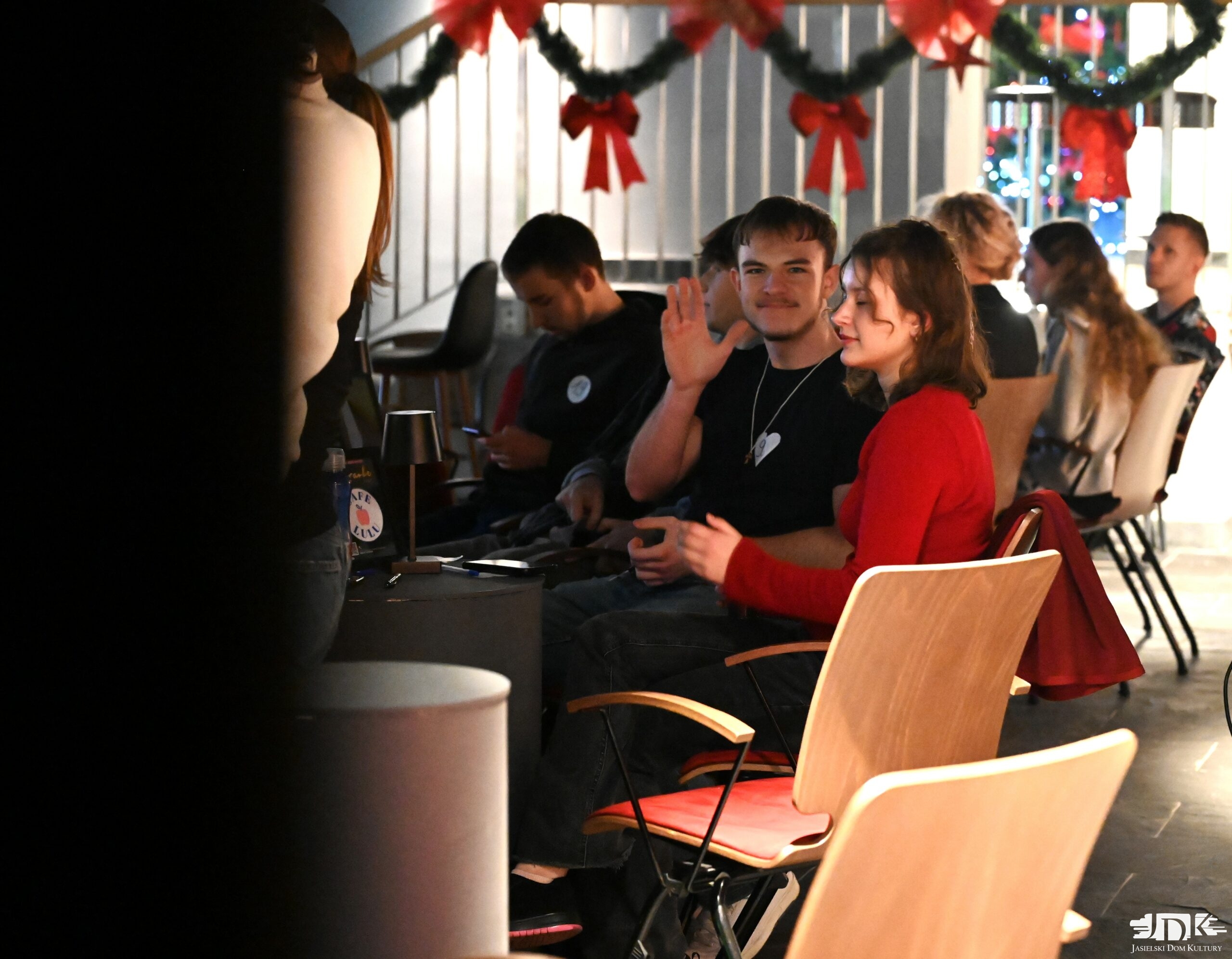 machający do obiektywu chłopak w czarnej koszulce, obok dziewczyna w czerwonej bluzce