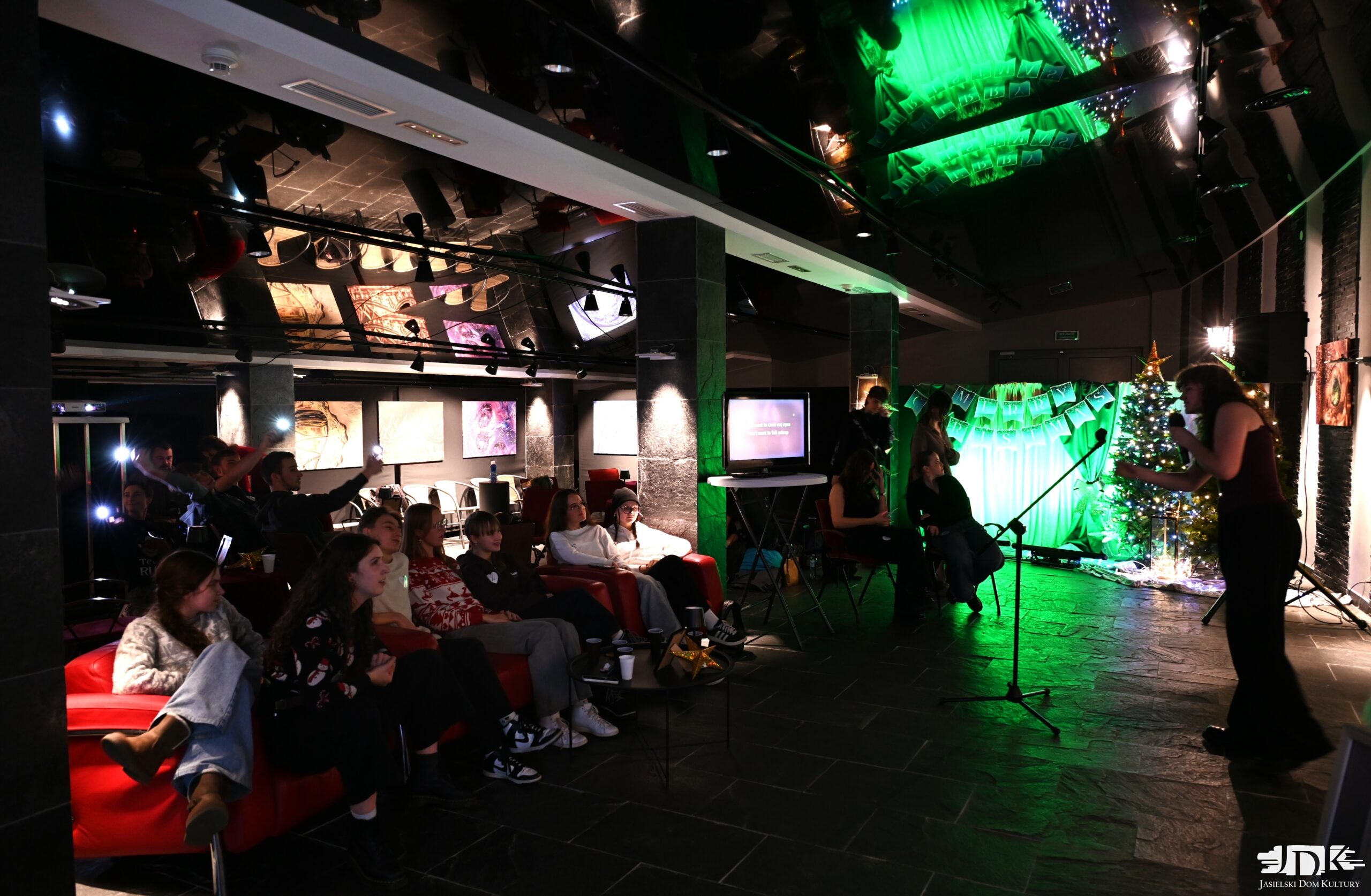 sala w której odbywa się domówka - czerwone kanapy, choinki, krzesełka i ekran.