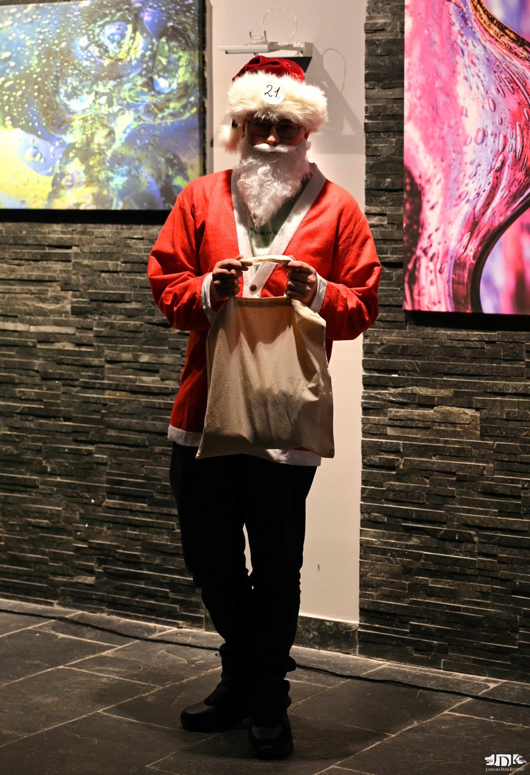 chłopiec przebrany za Mikołaja, trzymający w rękach torbę JDK a w niej nagroda za świąteczne przebranie w konkursie