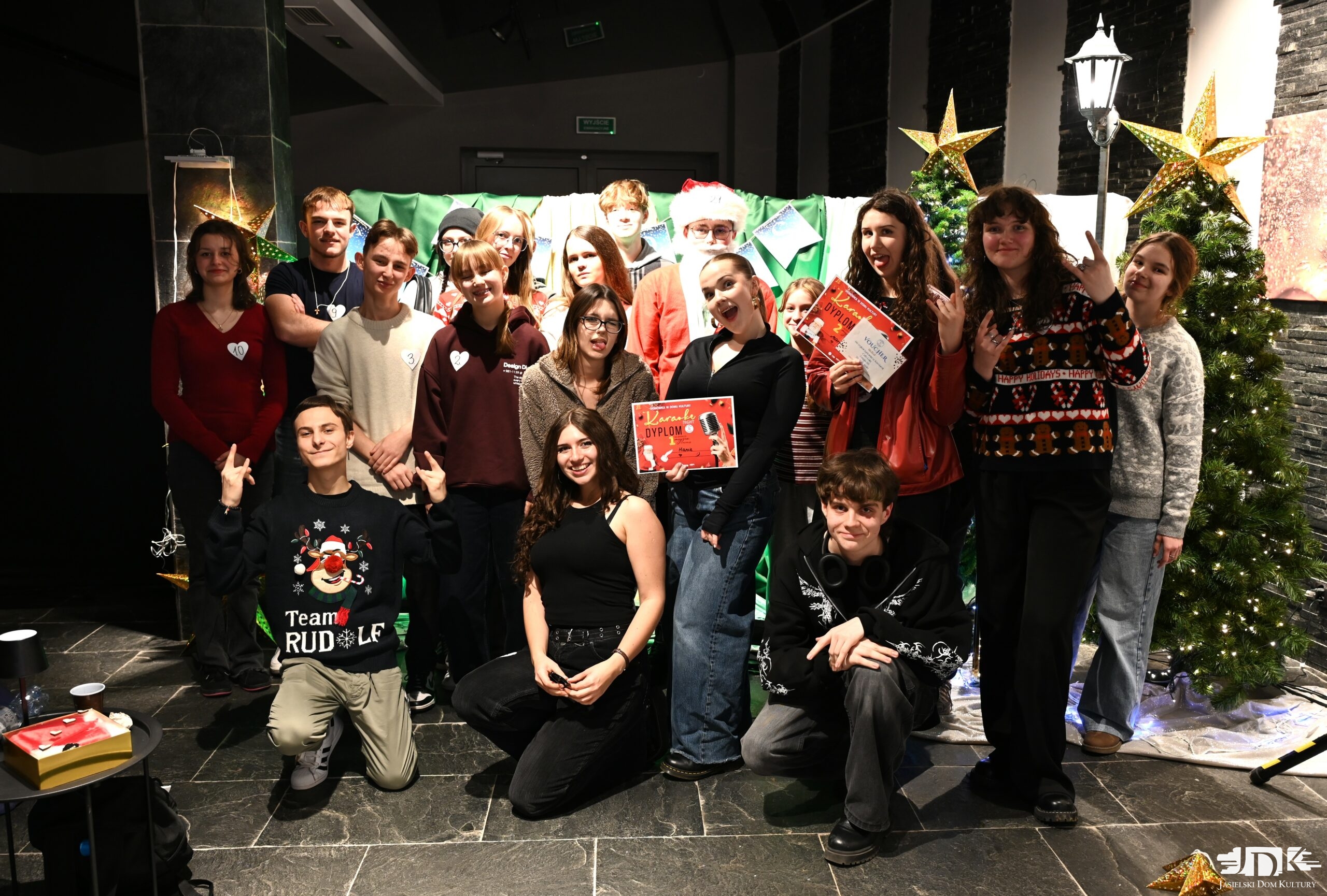 grupa uczestników karaoke na zimowej ściance, pozują uśmiechając się do aparatu. Niektórzy trzymają czerwone dyplomy