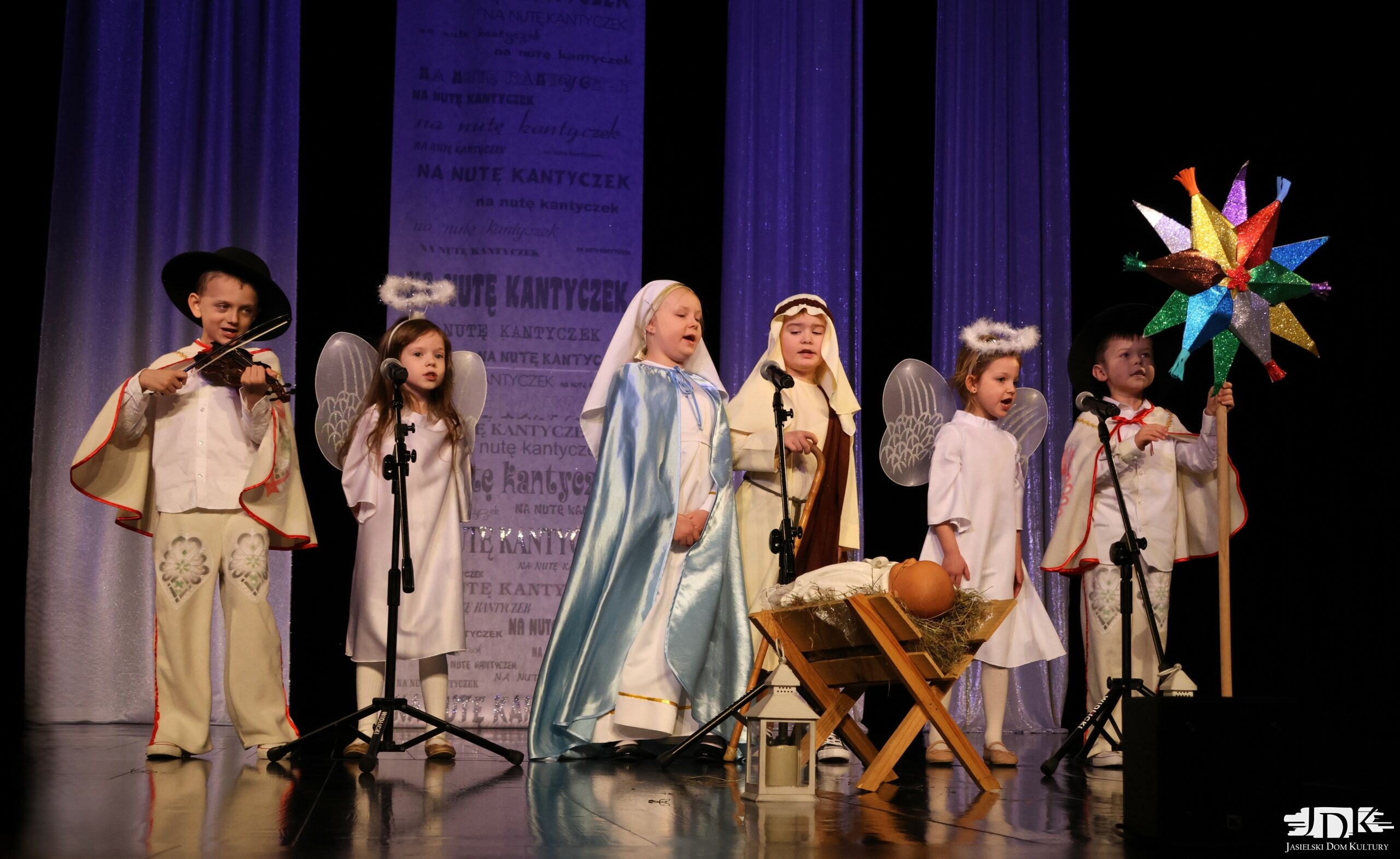 sześcioosobowy zespół przebrany za kolędników z gwiazdą. Przed nimi żłóbek z dzieciątkiem