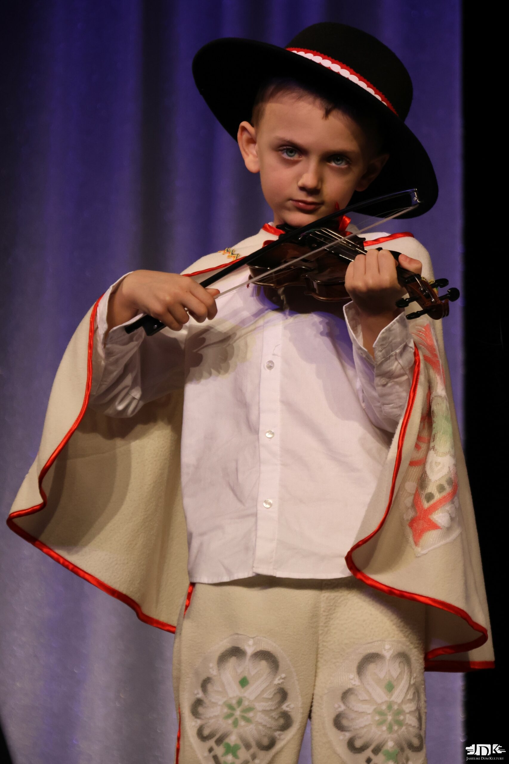 chłopiec w regionalnym stroju i kapeluszu gra na skrzypcach