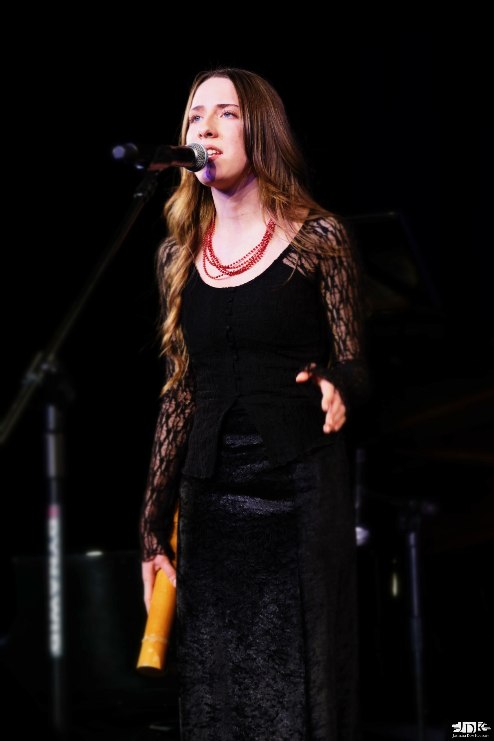 dziewczyna w czarnym stroju i czerwonych koralach, w ręce trzyma grzechotkę