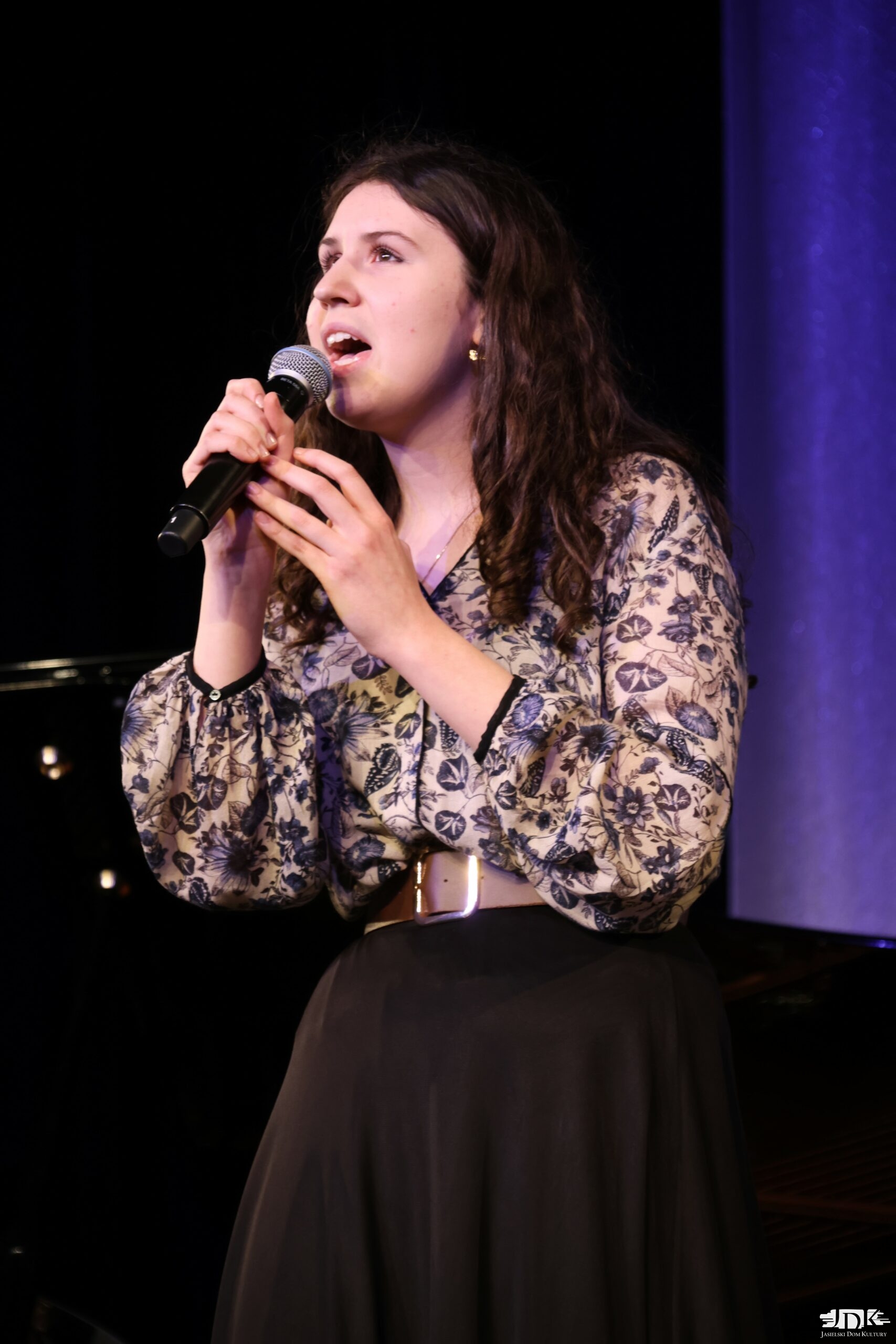 dziewczyna w czarnych spodniach i białej bluzce w granatowy motyw kwietny. Brązowy pasek z klamrą