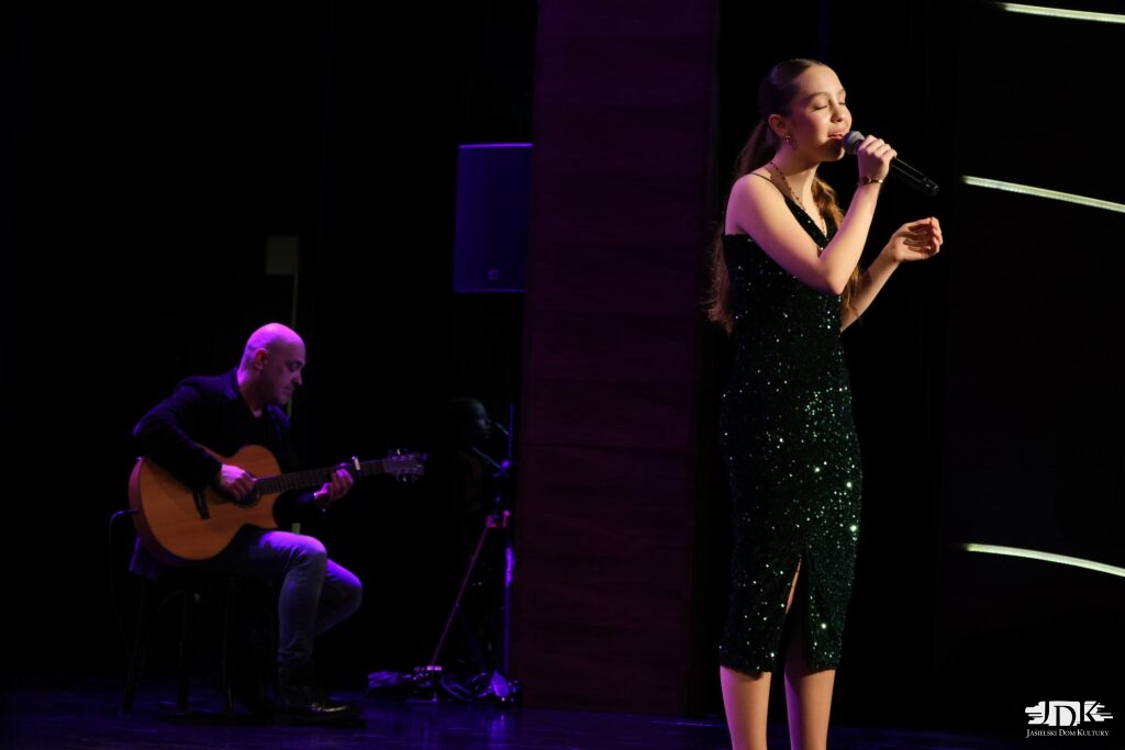 dziewczyna w cekinowej sukience, w tle akompaniator na gitarze