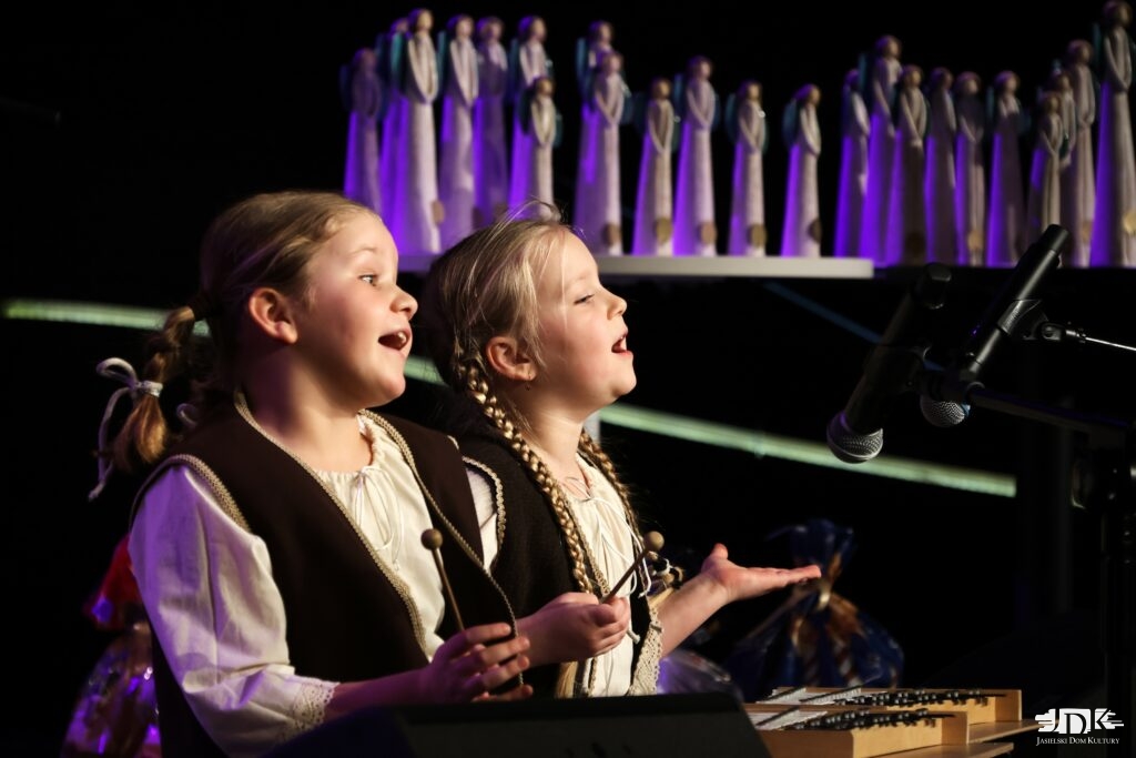 dwie dziewczynki w strojach ludowych siedzą i grają na cymbałkach