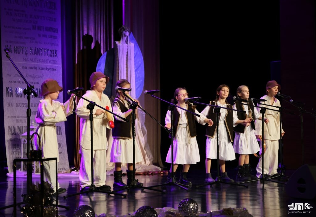 siedmioosobowy zespół w białych ubraniach i kożuszkach oraz chłopcy w brązowych czapkach